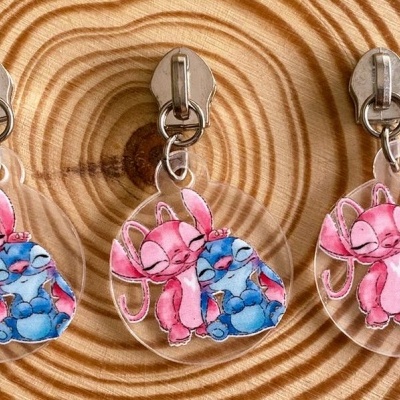 Três porta-chaves com desenho de coelho rosa e criatura azul abraçados em superfície de madeira.