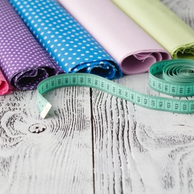 Rolos de tecido colorido e fita métrica verde sobre madeira branca