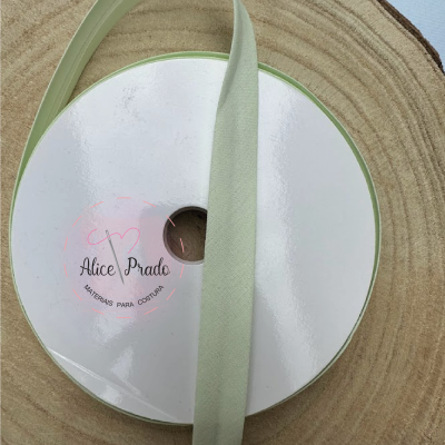 Rolo de fita têxtil verde claro com etiqueta Alice Prado sobre superfície de madeira