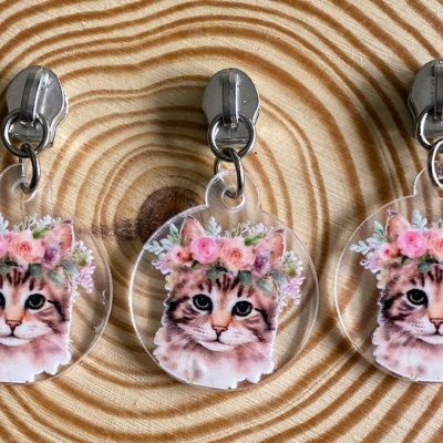 Três porta-chaves transparentes com imagem de gato com coroa de flores sobre superfície de madeira