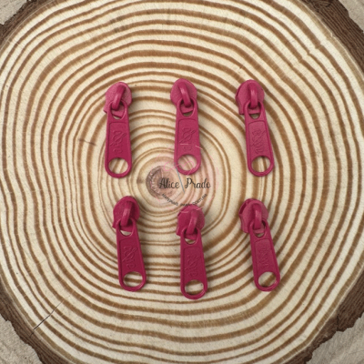 Seis pegas de zíper cor-de-rosa sobre fundo de madeira com padrão de anéis