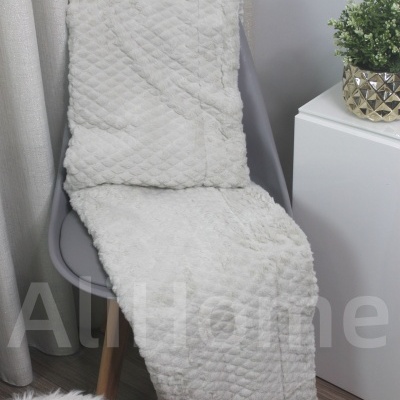 Cobertor branco acolchoado numa cadeira cinza com cortinas e planta ao lado