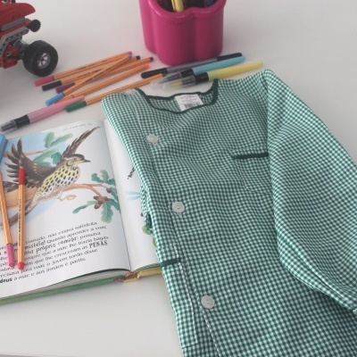 blusa infantil verde xadrez com livro e brinquedos sobre mesa branca