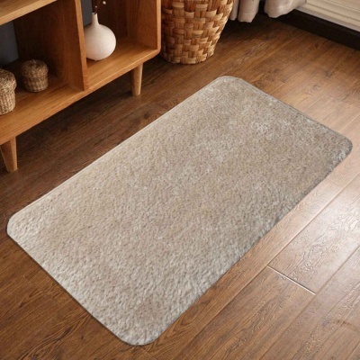 Tapete rectangular bege sobre chão de madeira ao lado de estante com objetos e cesto.