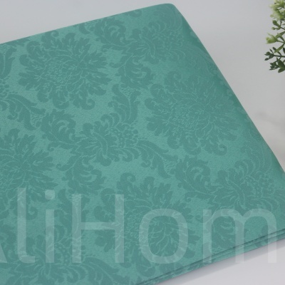 Capa de tecido verde água com padrão floral em relevo e vaso decorativo ao lado