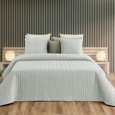 Cama com colcha cinzenta clara em padrão de chevrons e almofadas, ao lado mesas de cabeceira com lâmpadas.