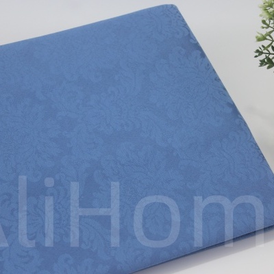 Tecido azul com padrão floral subtil ao lado de vaso prateado com planta