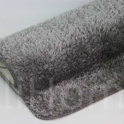 Tapete cinza de pelo alto enrolado ao lado de planta decorativa