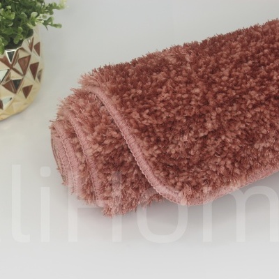 Tapete felpudo castanho avermelhado enrolado ao lado de vaso dourado com planta