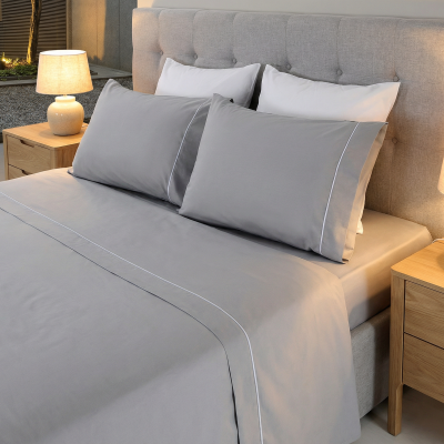 Roupa de cama cinzenta com linhas brancas numa cama com cabeceira estofada e mesas de cabeceira com abajures