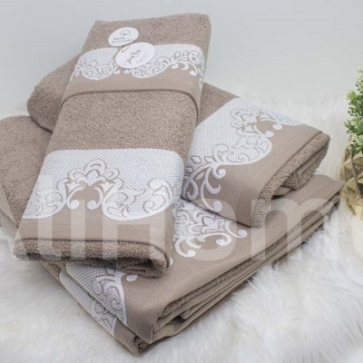 Conjunto de toalhas bege e castanho claro com bordados brancos e planta em vaso dourado