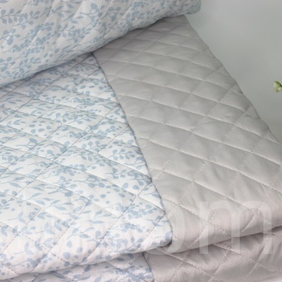 Colchão cinzento acolchoado com edredão floral azul claro e branco e vaso dourado com planta