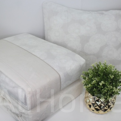 Conjunto de roupa de cama bege com padrão floral ao lado de vaso dourado com planta verde