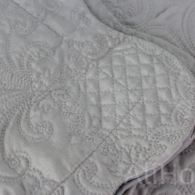 Colcha cinzenta com padrão bordado em relevo e acabamento arredondado