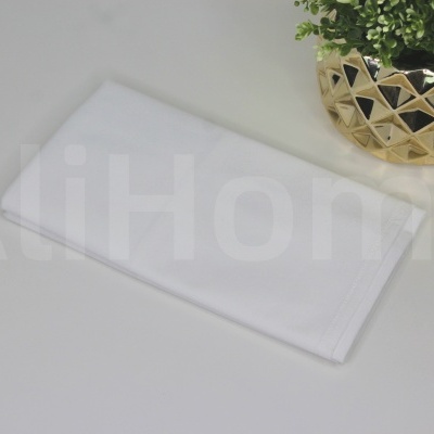 Toalha branca dobrada sobre mesa branca com vaso dourado e planta verde artificial