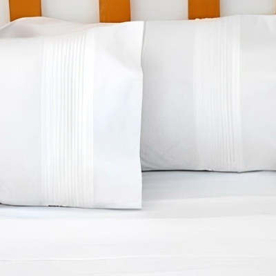 Frontal de duas fronhas e lençol branco sobre cama de madeira clara