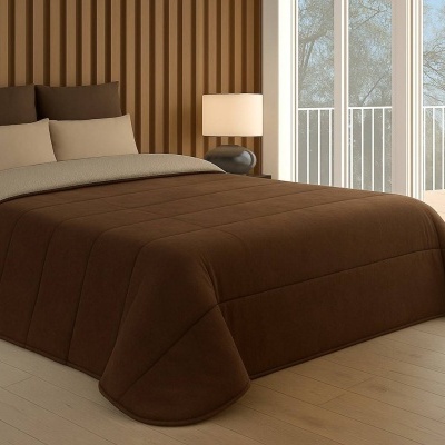 Cama com edredão castanho e almofadas bege e castanho numa sala com parede de madeira e janela grande