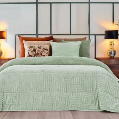 Cama de casal com edredão verde claro texturizado, almofadas castanhas e verdes, mesas de cabeceira com candeeiros e planta verde ao lado