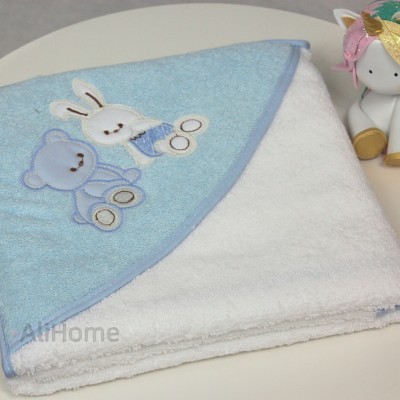 Toalha de banho branca com capuz azul e figuras bordadas de coelho e urso, junto a boneco de unicórnio