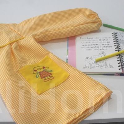 Vestido infantil amarelo xadrez com bolso e desenho de raposa ao lado de caderno e lápis de cor