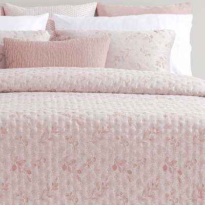Colcha e almofadas rosa claro com padrão floral em relevo numa cama