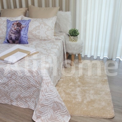 Cama com colcha bege, almofada com gato e tapete bege ao lado