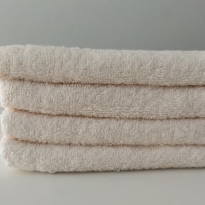 Quatro toalhas brancas empilhadas sobre superfície branca.