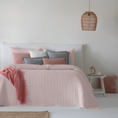 Cama com colcha rosa clara e almofadas coloridas num quarto minimalista