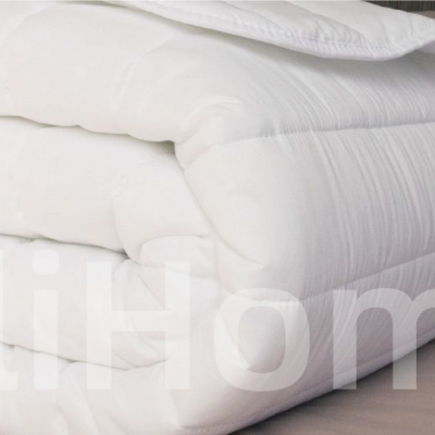 Edredão branco acolchoado dobrado sobre cama com lençol cinza claro