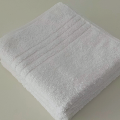 Toalha branca felpuda com riscas em relevo sobre fundo cinzento claro