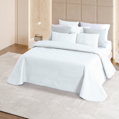 Cama branca com edredão e almofadas em quarto com carpete bege e parede acolchoada