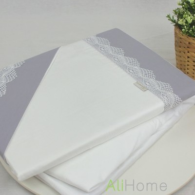 Tecido para cama branco com detalhes cinza e bordados rendados ao lado de planta e folhas secas