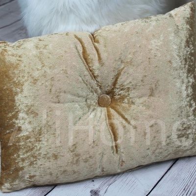 Almofada dourada aveludada com botão central sobre chão de madeira clara