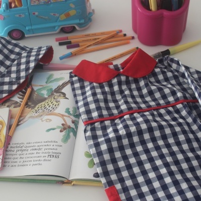 Vestido xadrez azul branco com gola vermelha, chapéu xadrez, livro aberto e lápis sobre mesa branca