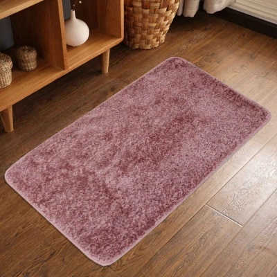 Tapete rectangular cor de rosa felpudo sobre chão de madeira numa divisão interior