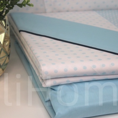 Roupas de cama azuis e brancas com padrão de bolinhas e vaso dourado com planta