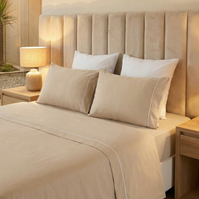 Cama feita com roupa de cama bege e almofadas num quarto com decoração clara e candeeiros nas mesas de cabeceira.