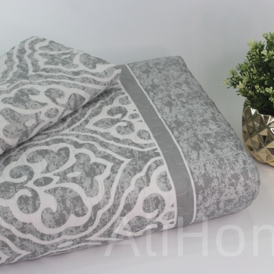 Toalhas cinzentas e brancas com padrão decorativo e vaso dourado com planta artificial