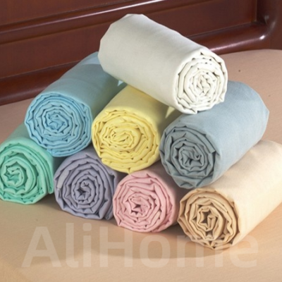 Oito lençóis de cama enrolados em cores pastéis sobre cama com cabeceira de madeira