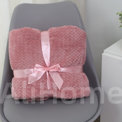 Manta rosa com laço em cadeira cinzenta junto a móvel branco e planta.