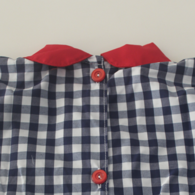 Peça de roupa com padrão xadrez azul e branco, botões vermelhos e gola vermelha