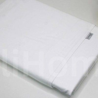 Lençol branco dobrado com etiqueta cinza junto a vaso decorativo dourado.