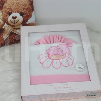 Toalha de bebé branca e rosa com bordado de flor e pássaro na caixa ao lado de imagem de ursinhos de pelúcia