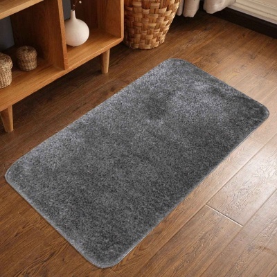 Tapete retangular cinza de pelo curto em chão de madeira, com canto arredondado