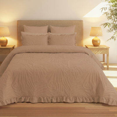 Conjunto de roupa de cama bege com padrão de folhas em quarto iluminado, com mesas de cabeceira de madeira, candeeiros dourados e planta numa jarra branca.