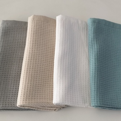 Quatro panos de cozinha dobrados em quatro cores diferentes sobre uma mesa branca