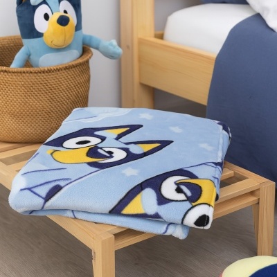 Manta azul com padrão de cães sobre banco de madeira em quarto infantil com peluche azul e bola colorida