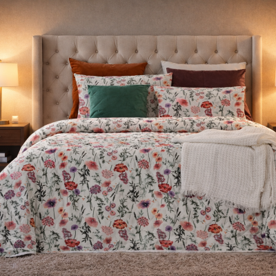 Cama com edredão floral, almofadas coloridas, manta branca e mesas de cabeceira com candeeiros em quarto acolhedor