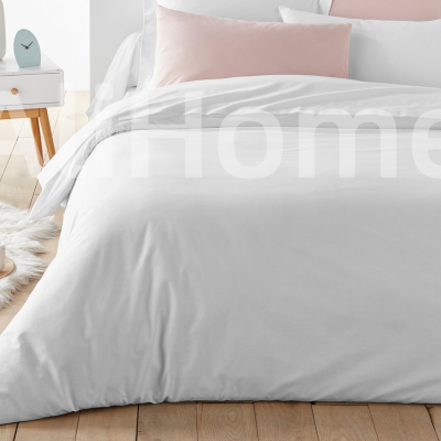 Cama com roupa de cama branca e almofadas rosa claro ao lado de candeeiro e tapete