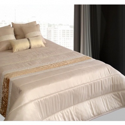 Colcha bege com detalhes dourados e almofadas combinando em cama